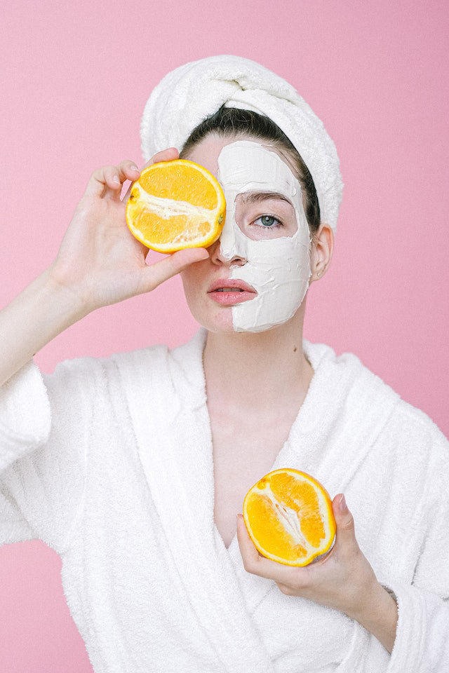 Vitamina-C mujer con crema en la cara mostrando una naranja